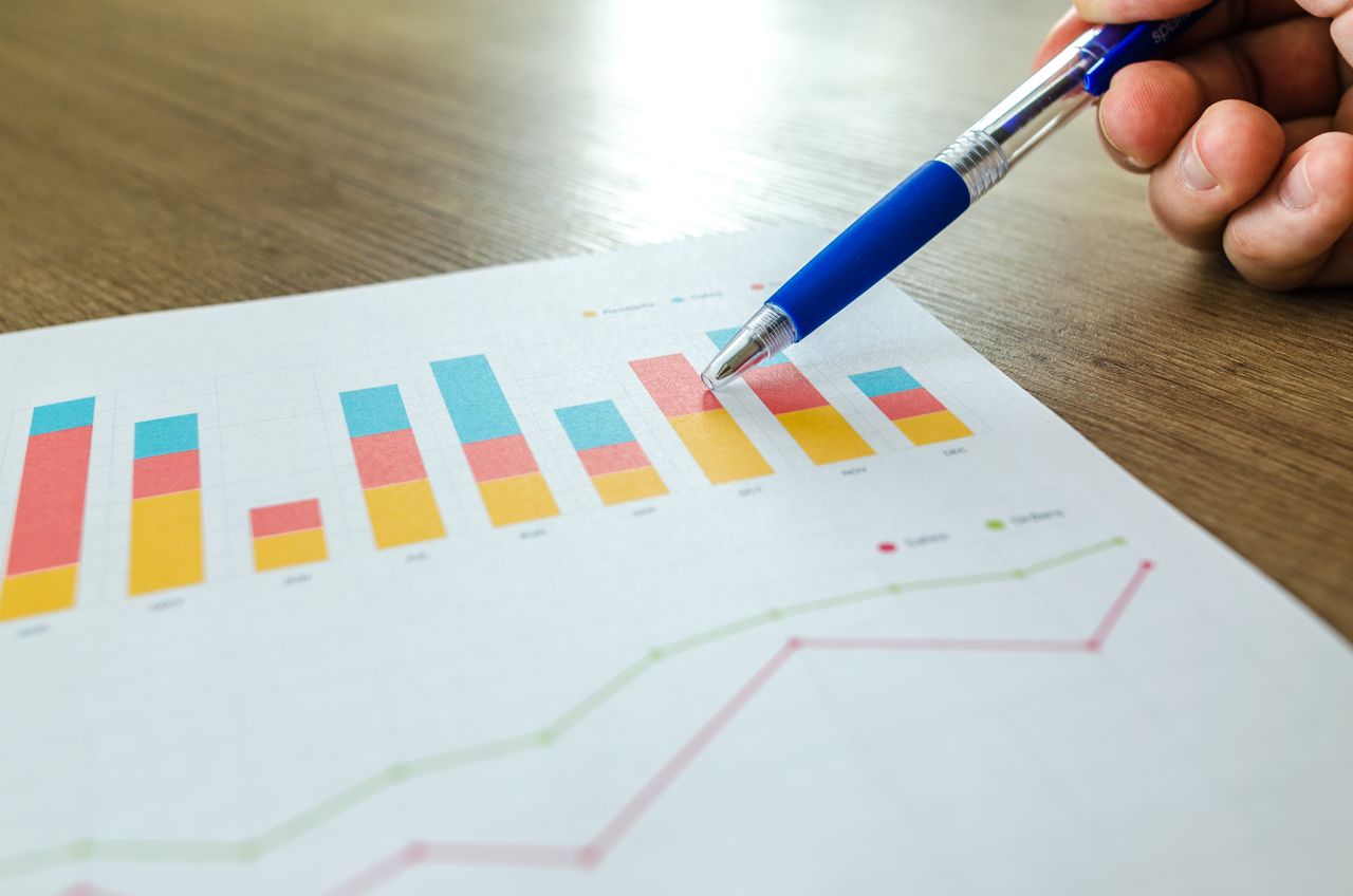 Vue rapprochée détaillée d’une main indiquant des graphiques colorés avec un stylo bleu sur une surface en bois.